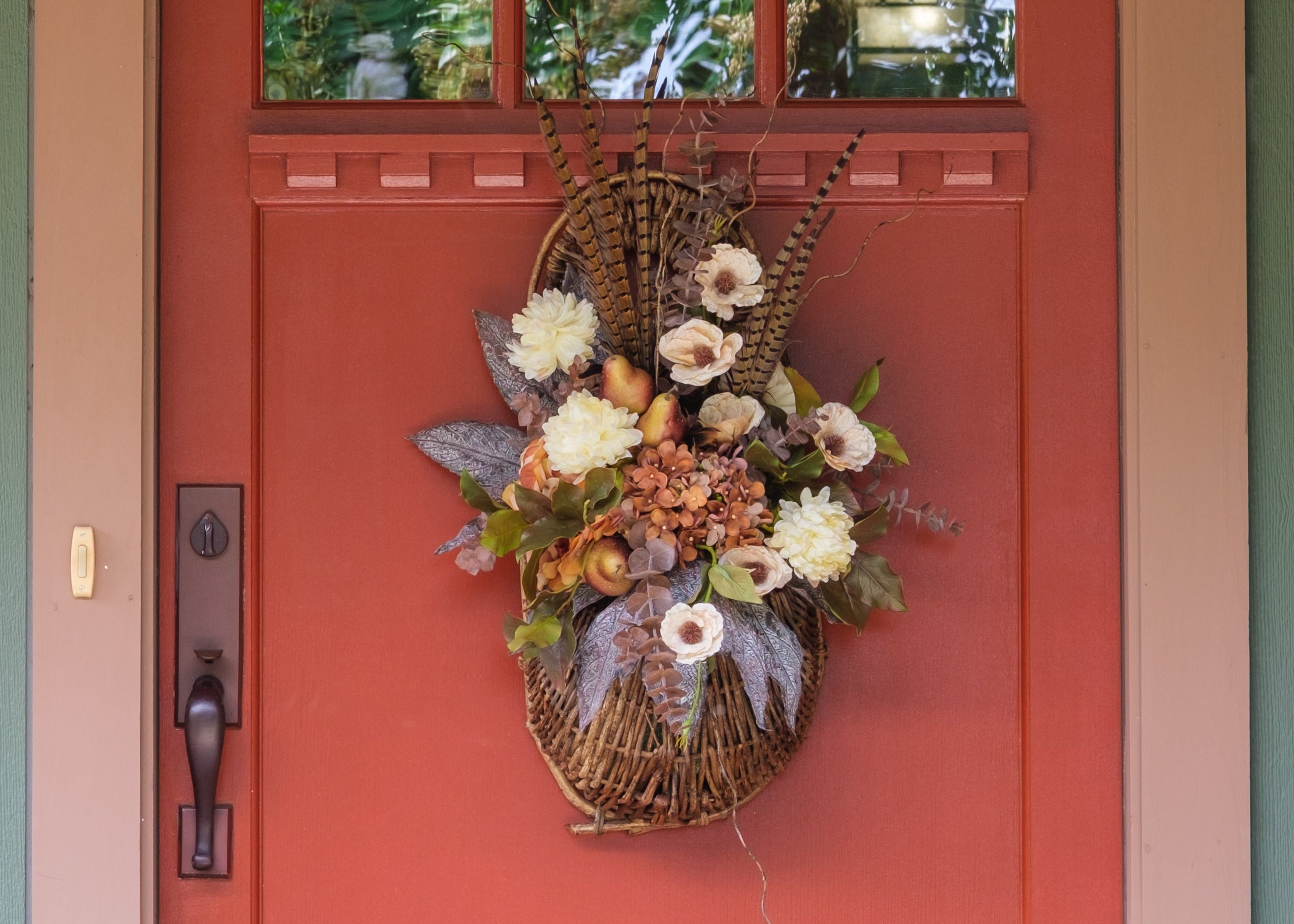 A rustic autumn wicker basket wall hanging filled with faux flowers and fall foliage, displayed on a red front door.